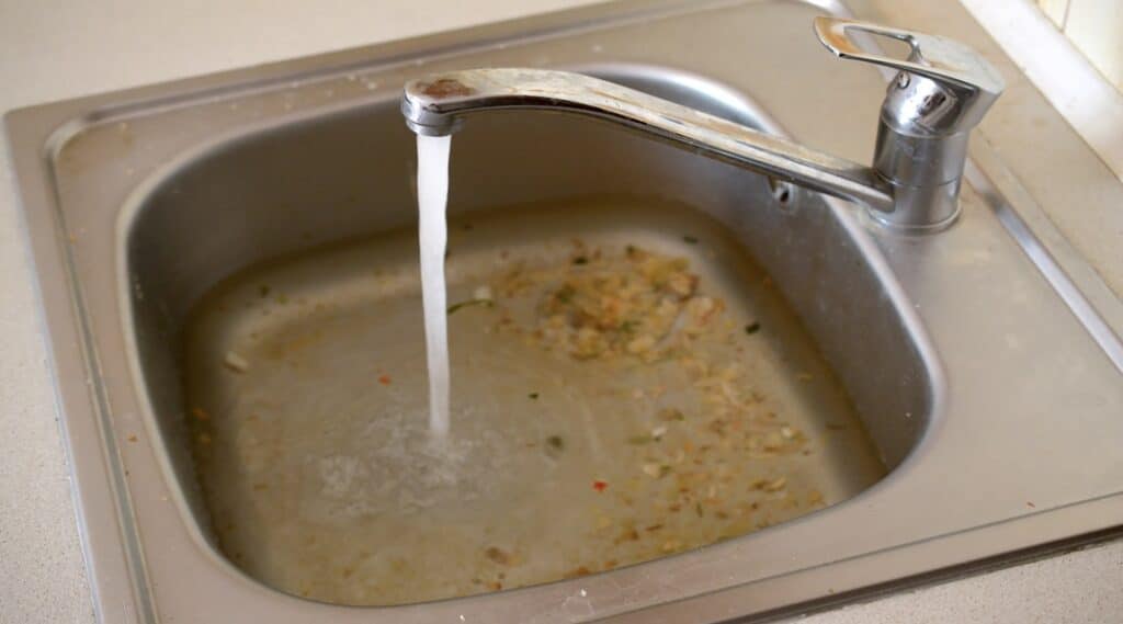 Stainless steel sink plug hole close up full of water and particles of food